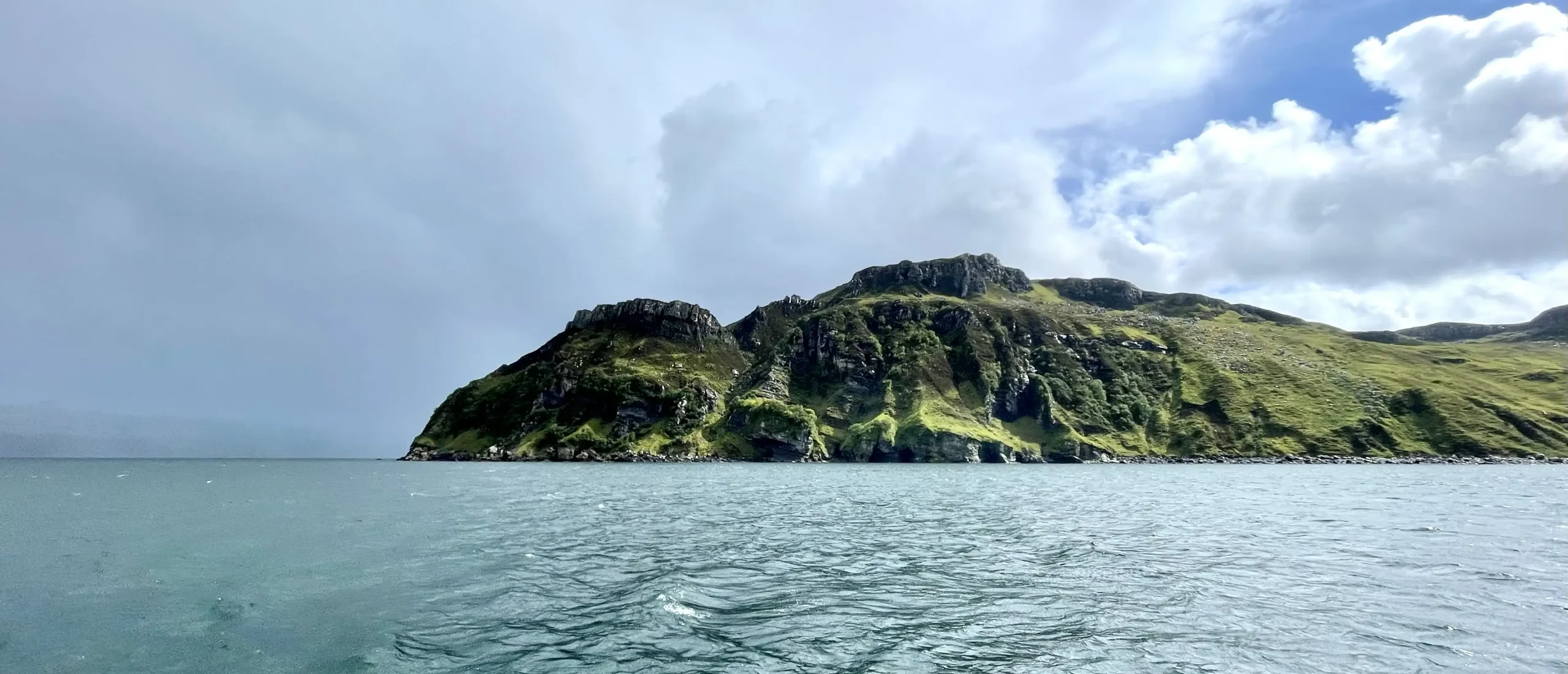 Die felsige grüne Insel Reviere erhebt sich aus dem blauen Wasser unter einem teilweise bewölkten Himmel.