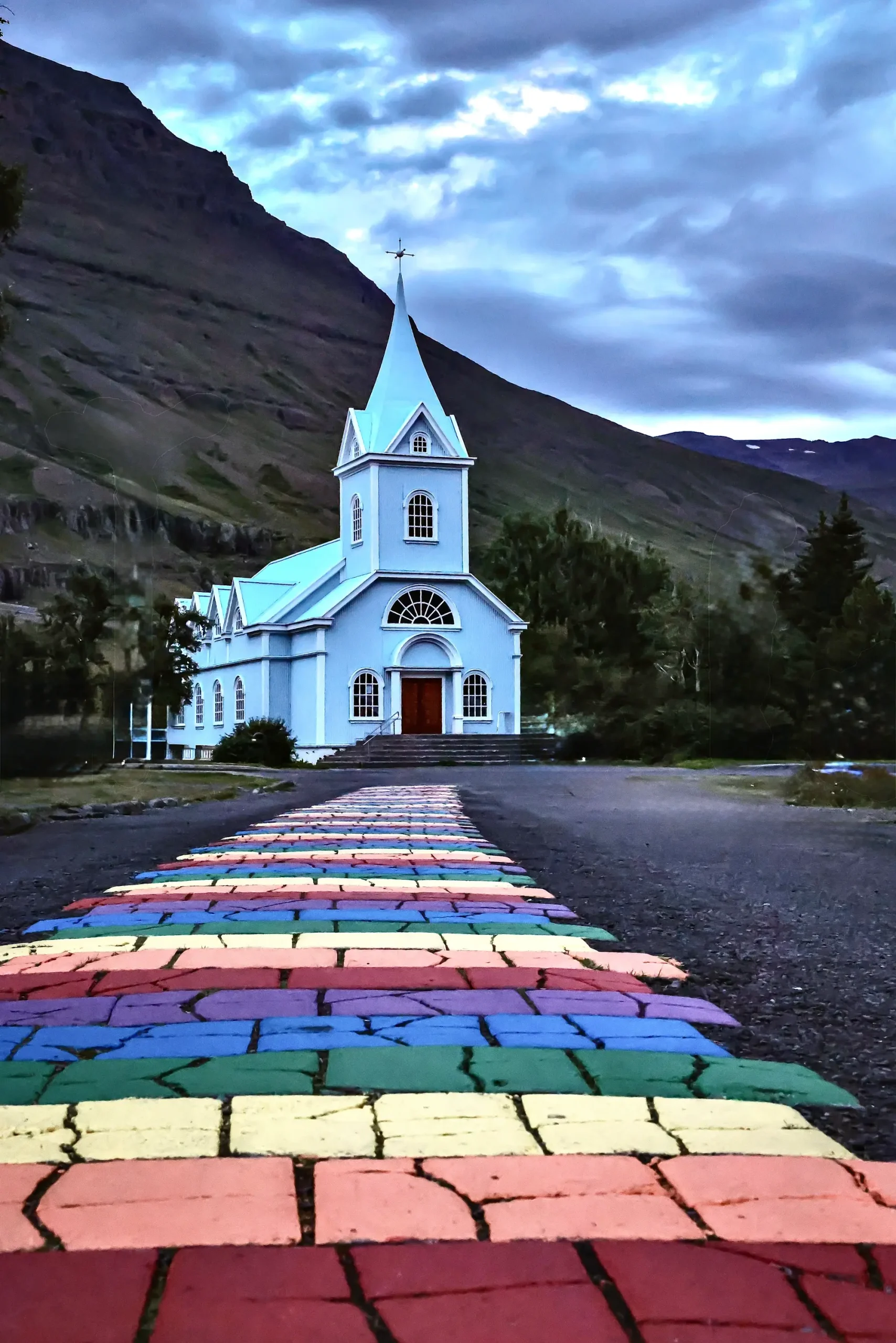 Eine blaue Kirche mit einem regenbogenfarbenen Weg, der zu ihrem Eingang führt, inmitten von Bergen.