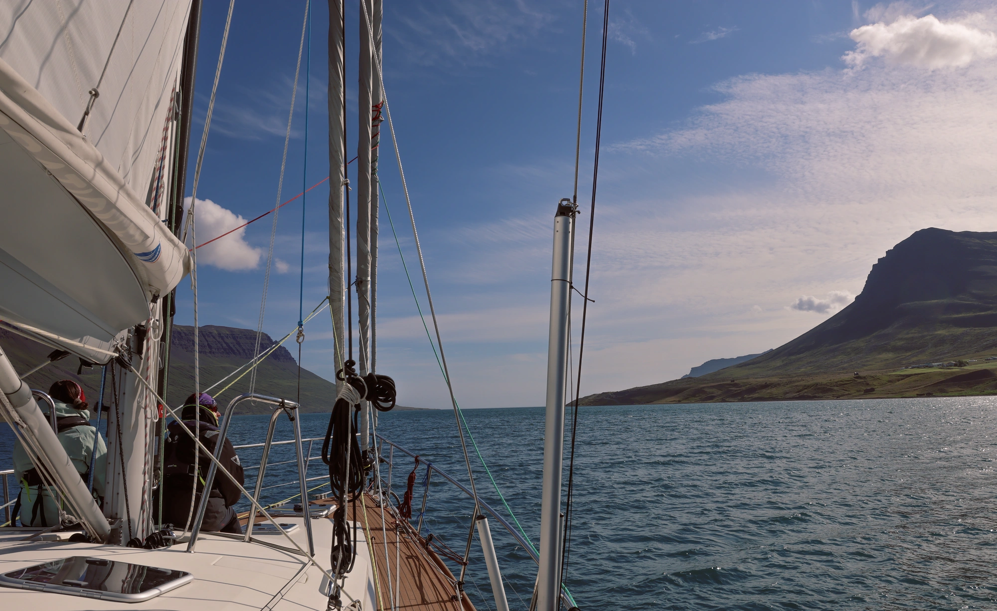 Blick von einem Segelboot auf dem Wasser in der Nähe von Bergen unter einem blauen Himmel mit Wolken.