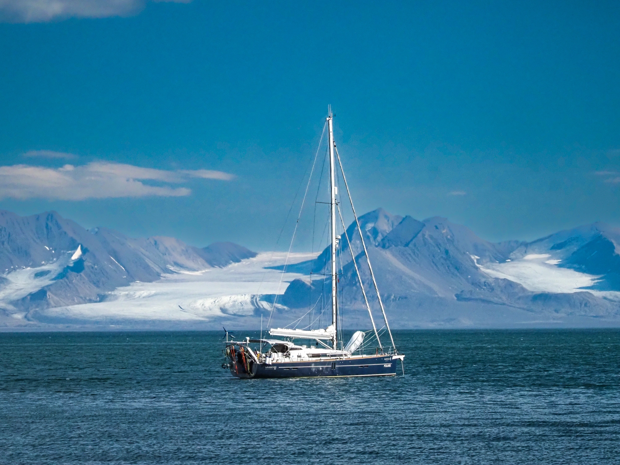 Segelboot auf ruhigem Wasser in der malerischen Reviere, schneebedeckte Berge unter einem blauen Himmel.