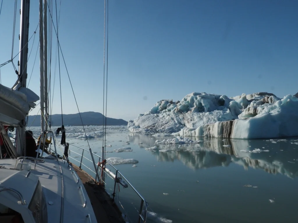 Ein Segelboot nähert sich einem großen Eisberg vor Spitzbergen in ruhigen, eisigen Gewässern bei klarem Himmel.